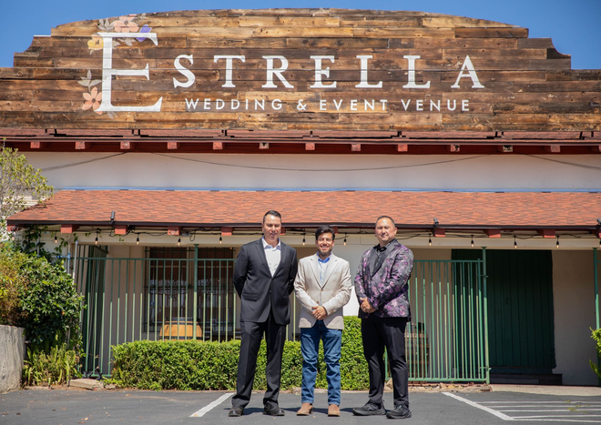 Three people standing outside Estrella Wedding Event Venue entrance under a wooden sign.