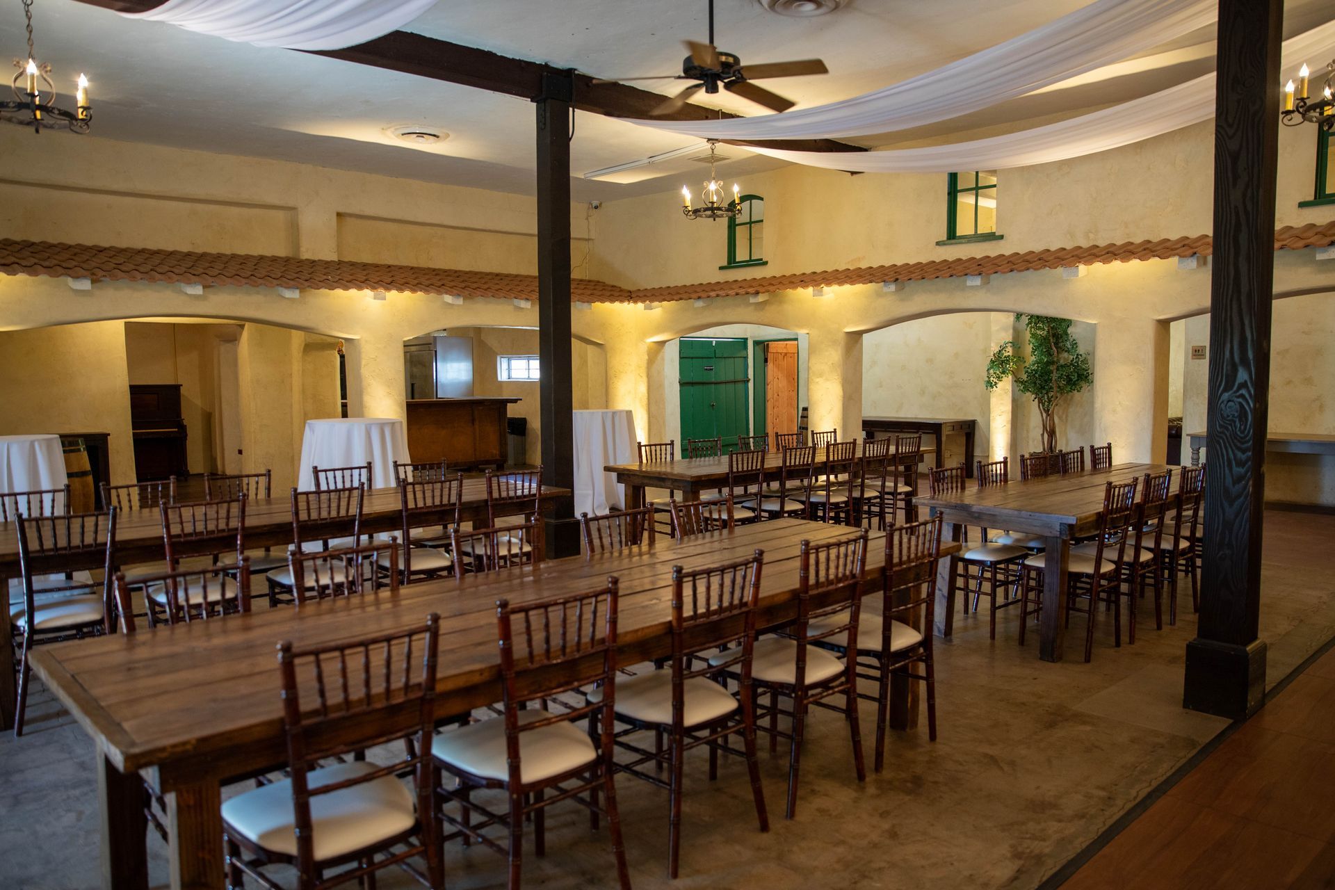 Empty banquet hall with wooden chairs and tables, beige walls, and dark ceiling beams