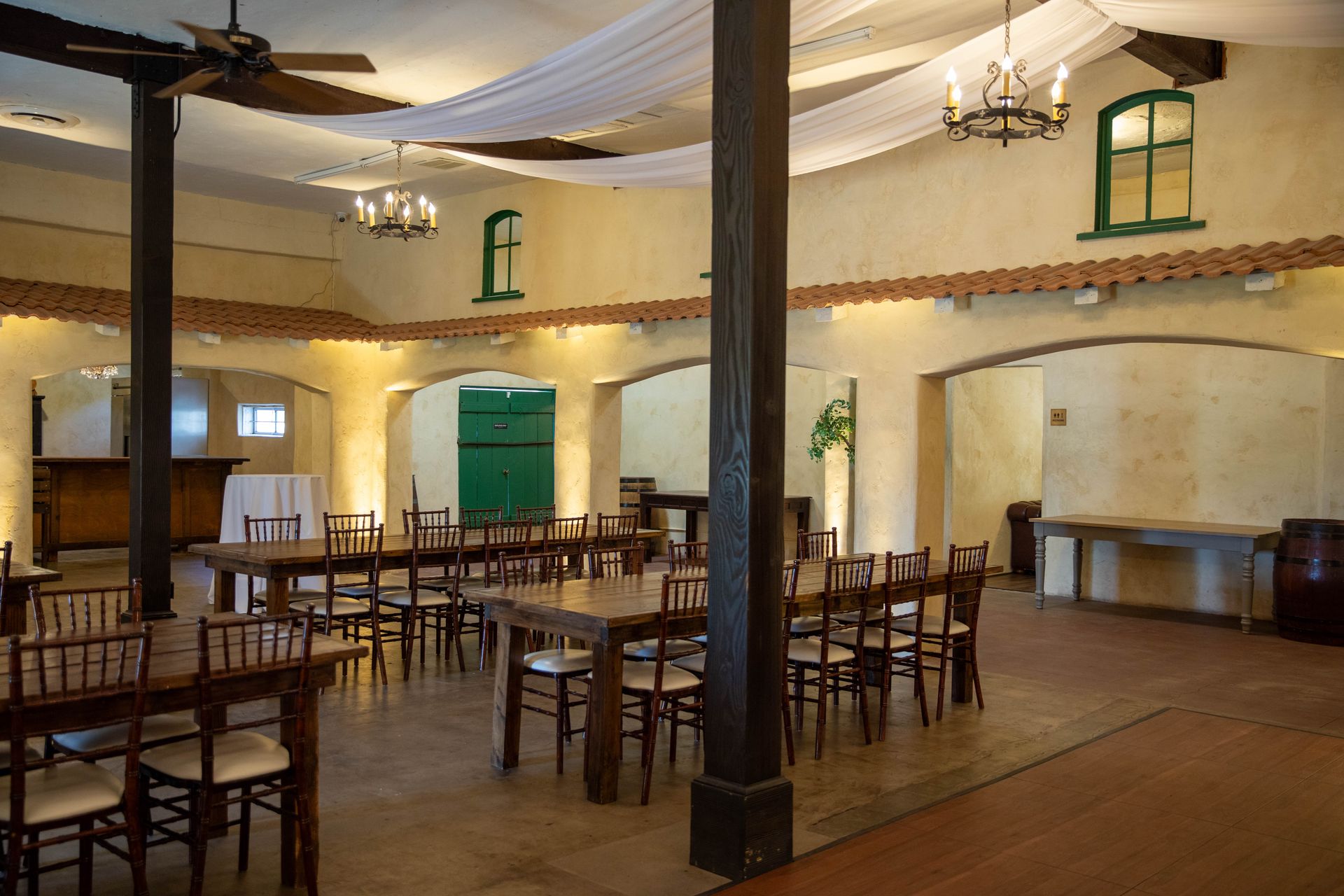 Empty banquet hall with wooden chairs and tables, white draped ceiling, and arched doorways.