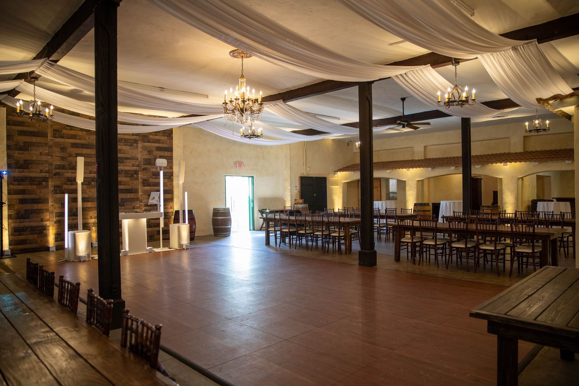 Empty banquet hall with draped ceiling, chandeliers, wooden floor, and rows of tables and chairs