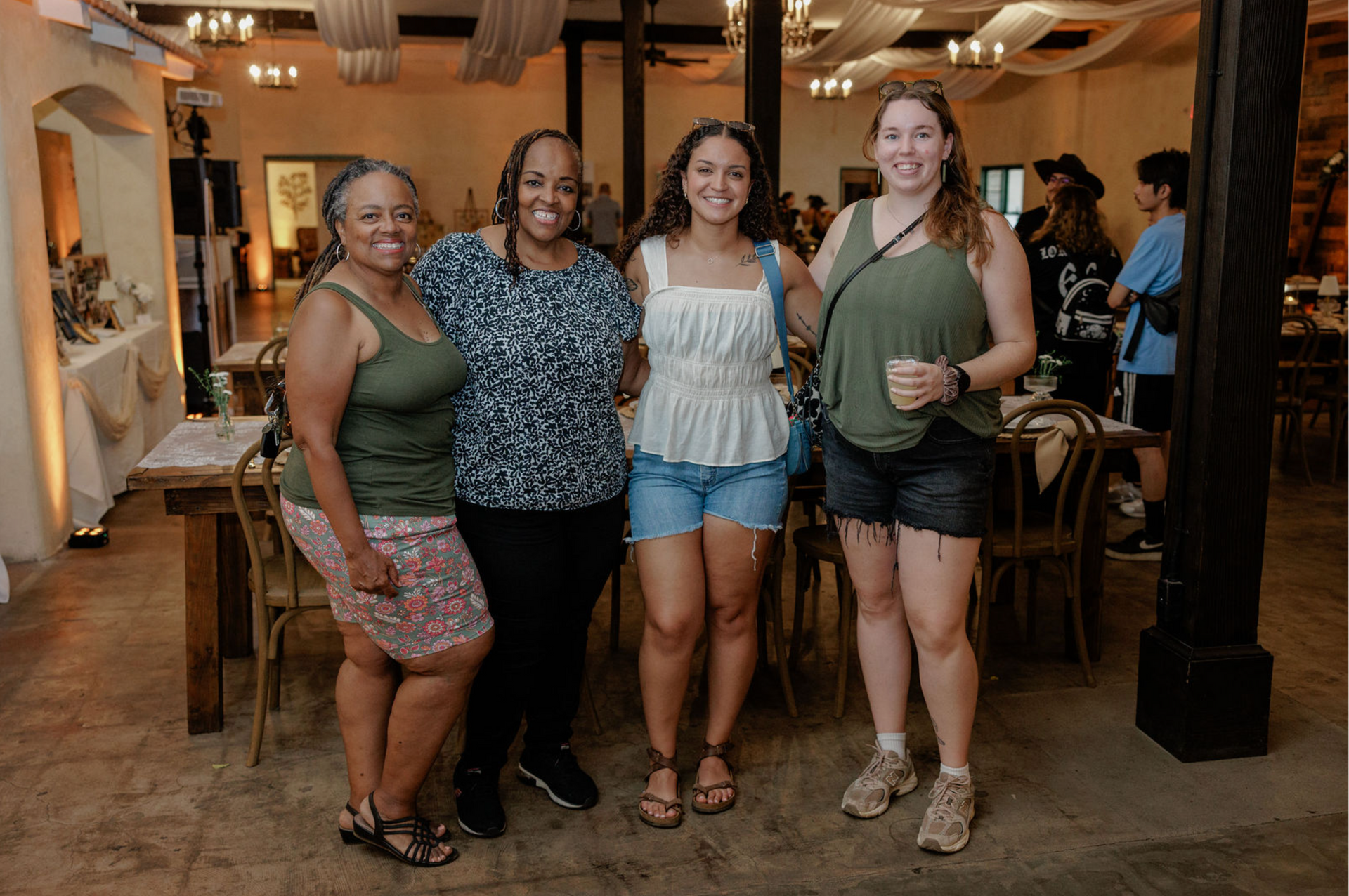 Four friends posing together in a warmly lit restaurant, smiling beside a table