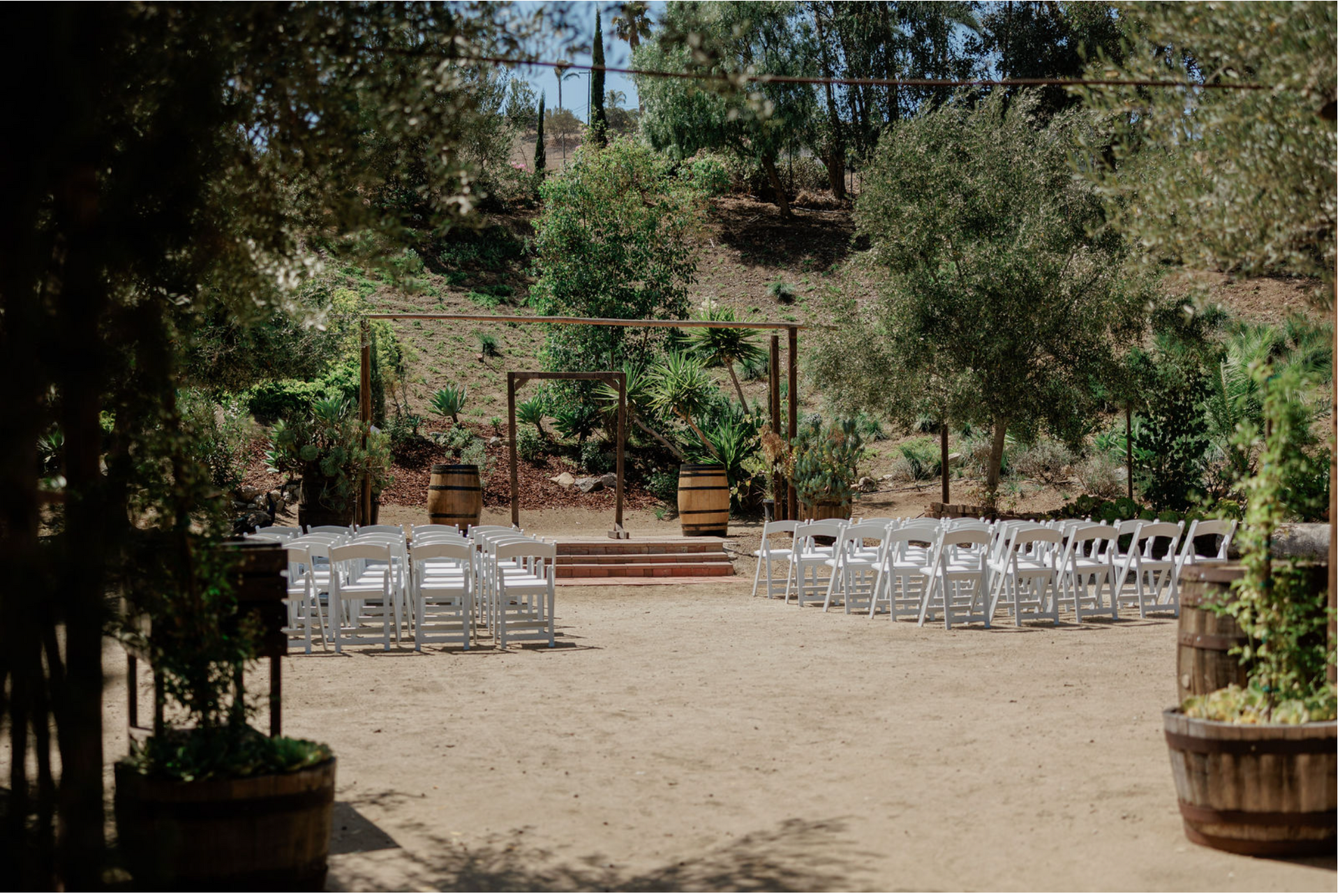 Outdoor wedding ceremony setup with white chairs and a small altar in a sandy garden clearing