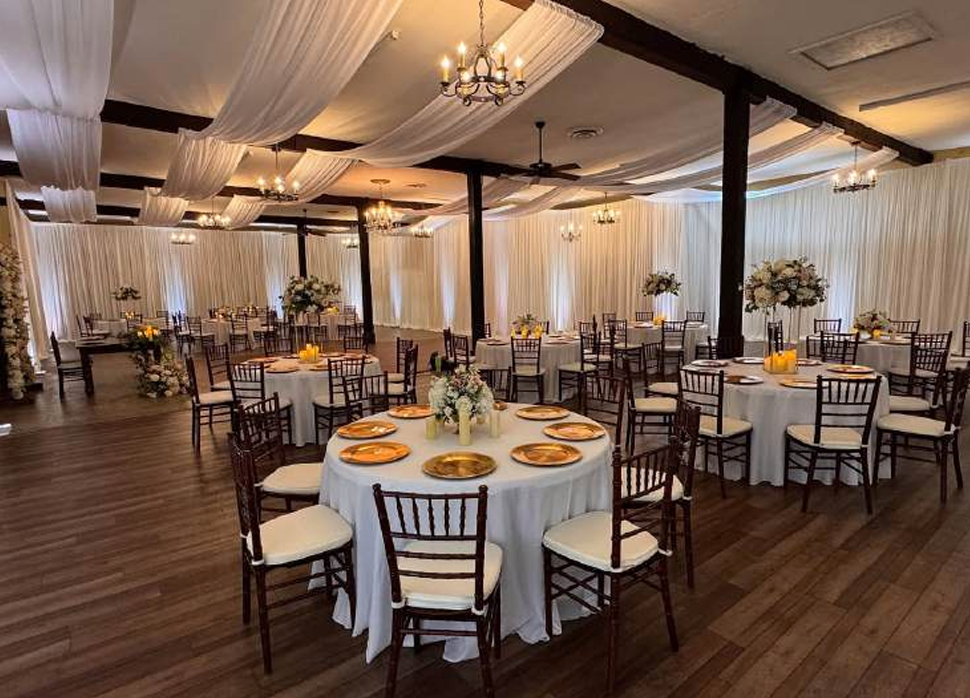 Elegant banquet hall with round tables, white chairs, and draped ceiling decor