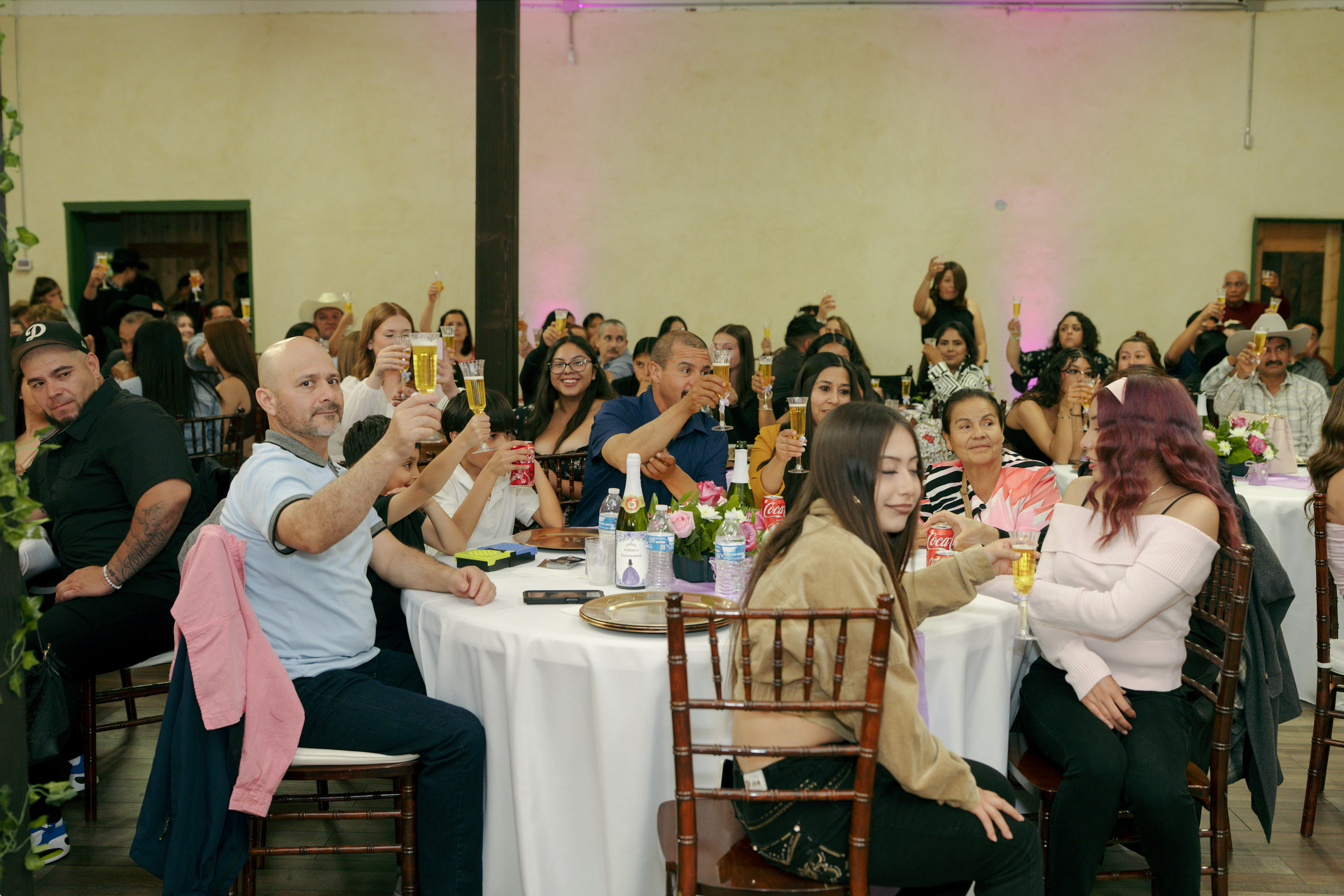 Guests seated at round tables applaud at a banquet in a warmly lit event hall.