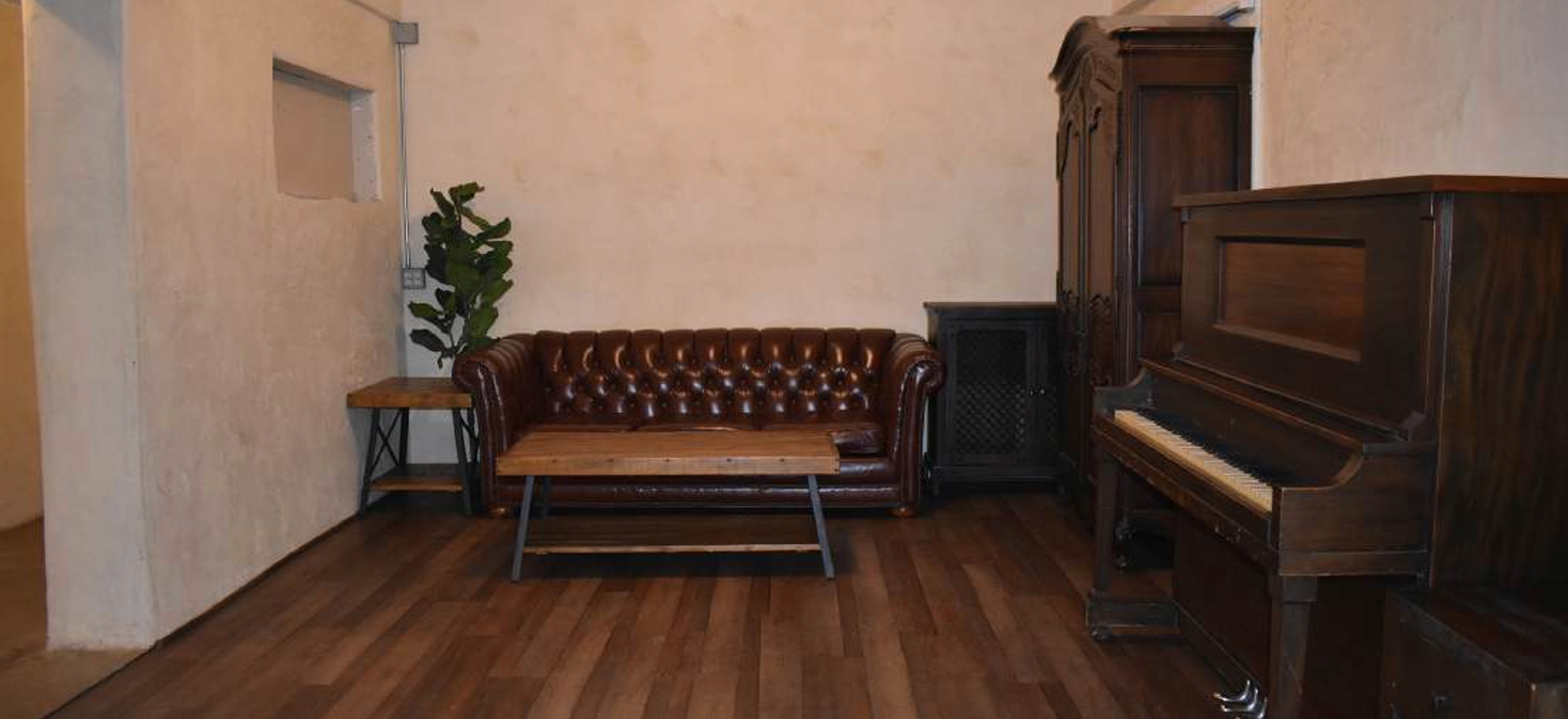 Empty room with a leather sofa, piano, cabinet, and potted plant on wood floors