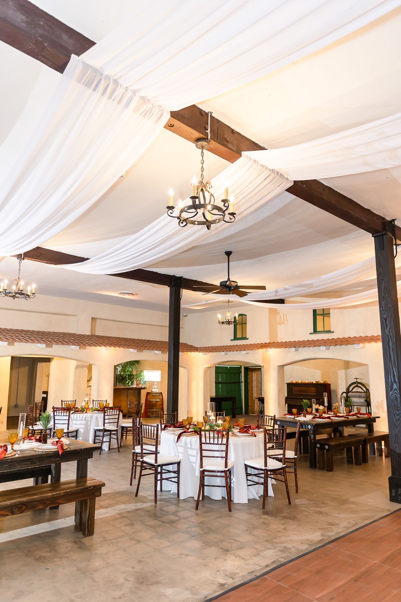 Elegant restaurant dining room with white draped ceiling, chandeliers, and wooden tables and chairs