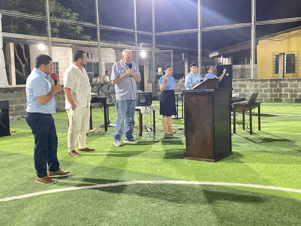 People standing and speaking at an outdoor pavilion podium at night