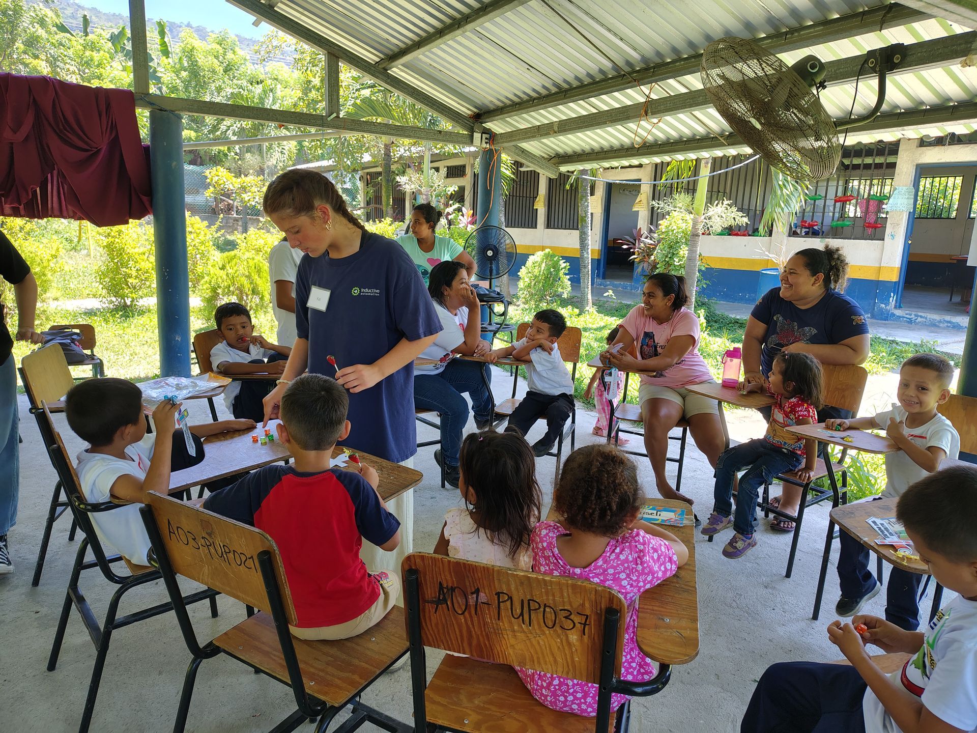 Teacher with children seated in a covered outdoor classroom, holding papers and working together