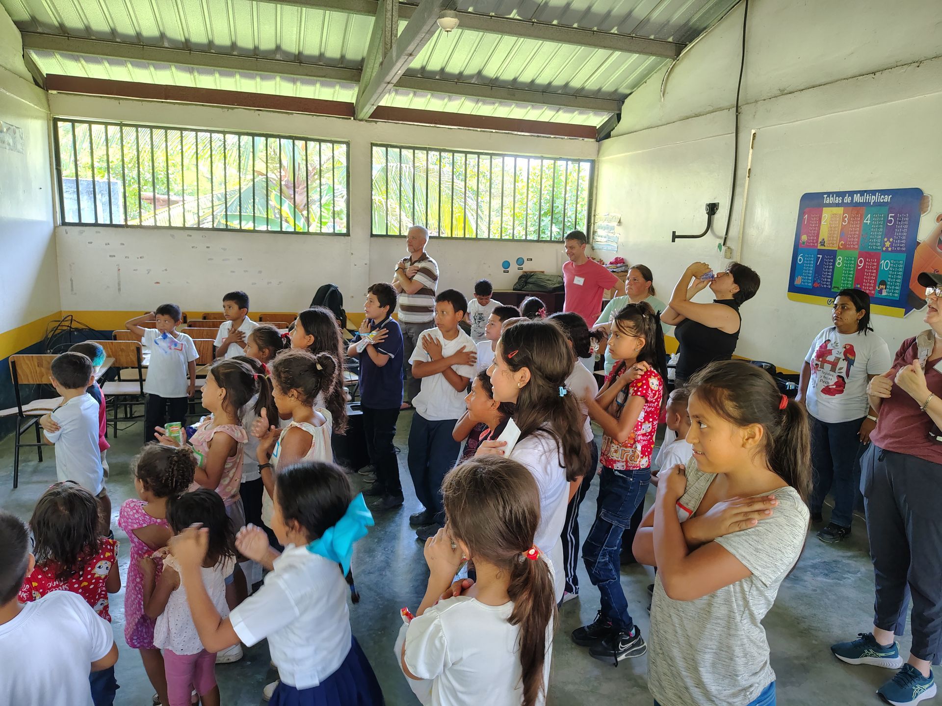 Children standing and listening in a classroom with bright walls and colorful posters
