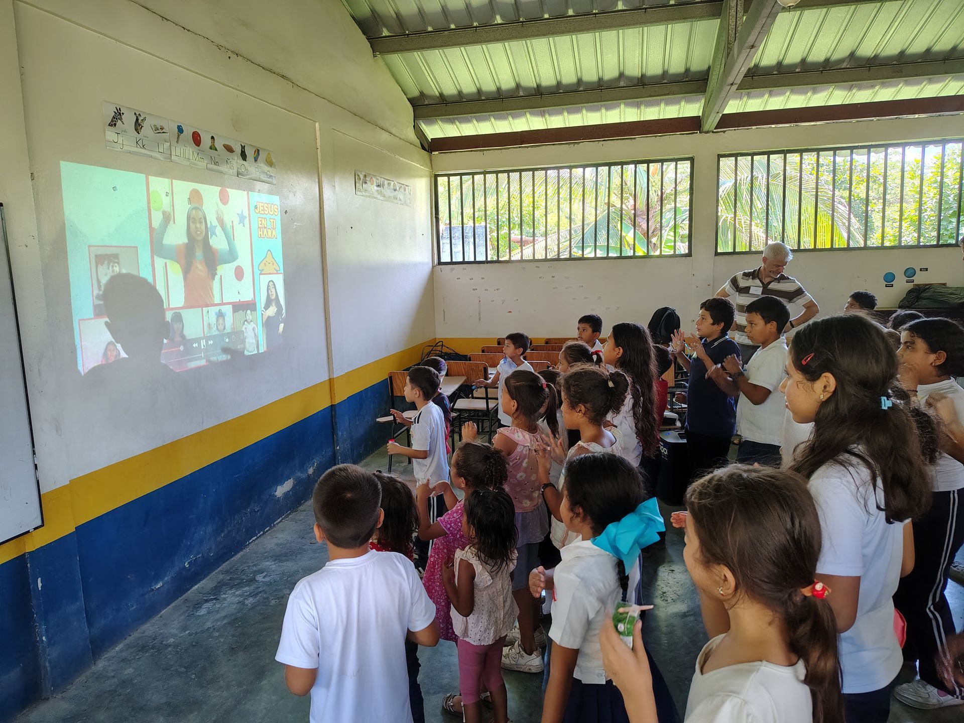 Children watching a projected lesson in a classroom with blue-and-yellow walls.