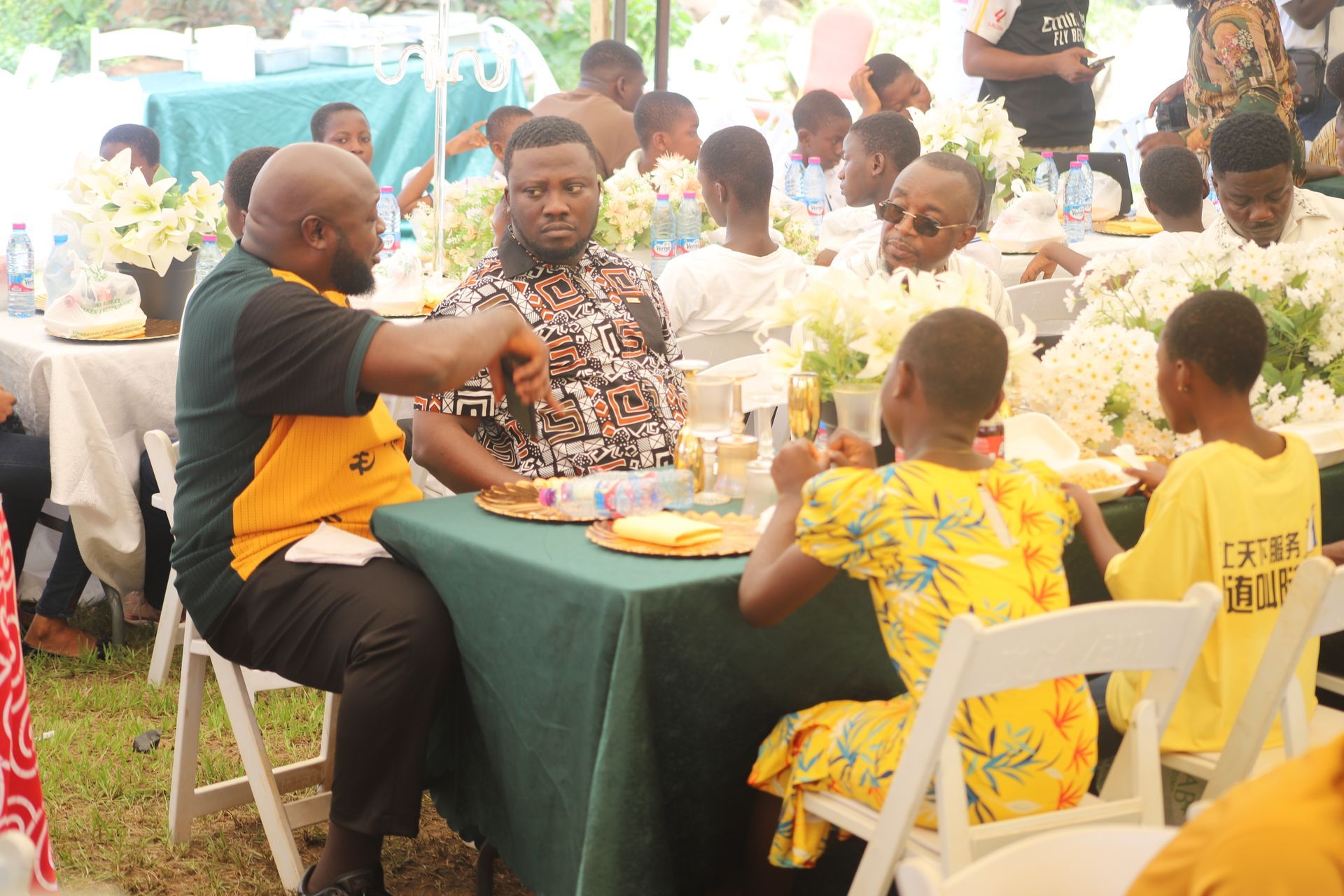 People seated around a table outdoors, sharing food and drinks at a social gathering.