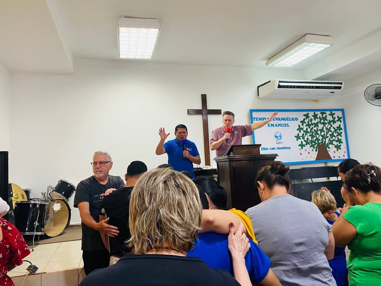 People gathered in a church hall with a speaker at a podium and a cross on the wall.