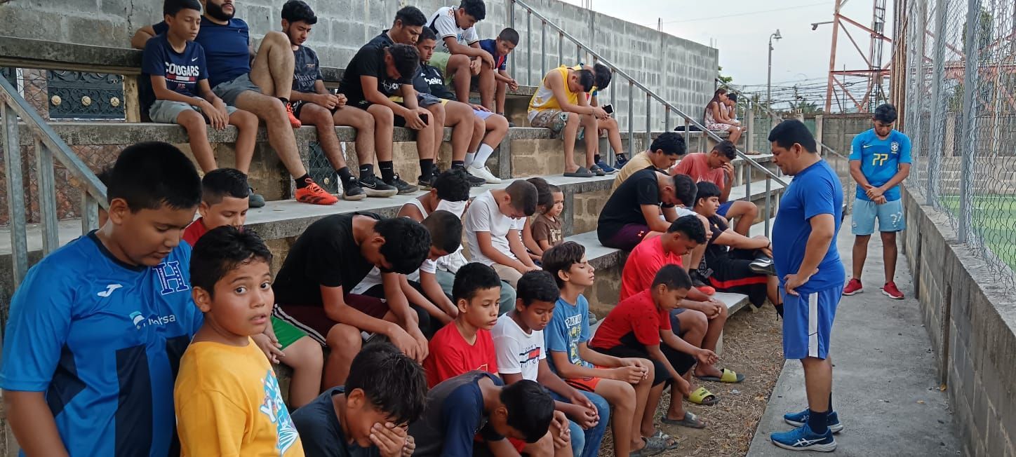 Group of spectators seated on bleachers watching a sports event, with a coach standing nearby.