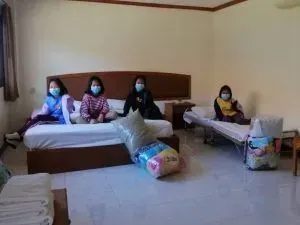 A group of people wearing face masks are sitting on beds in a hotel room.