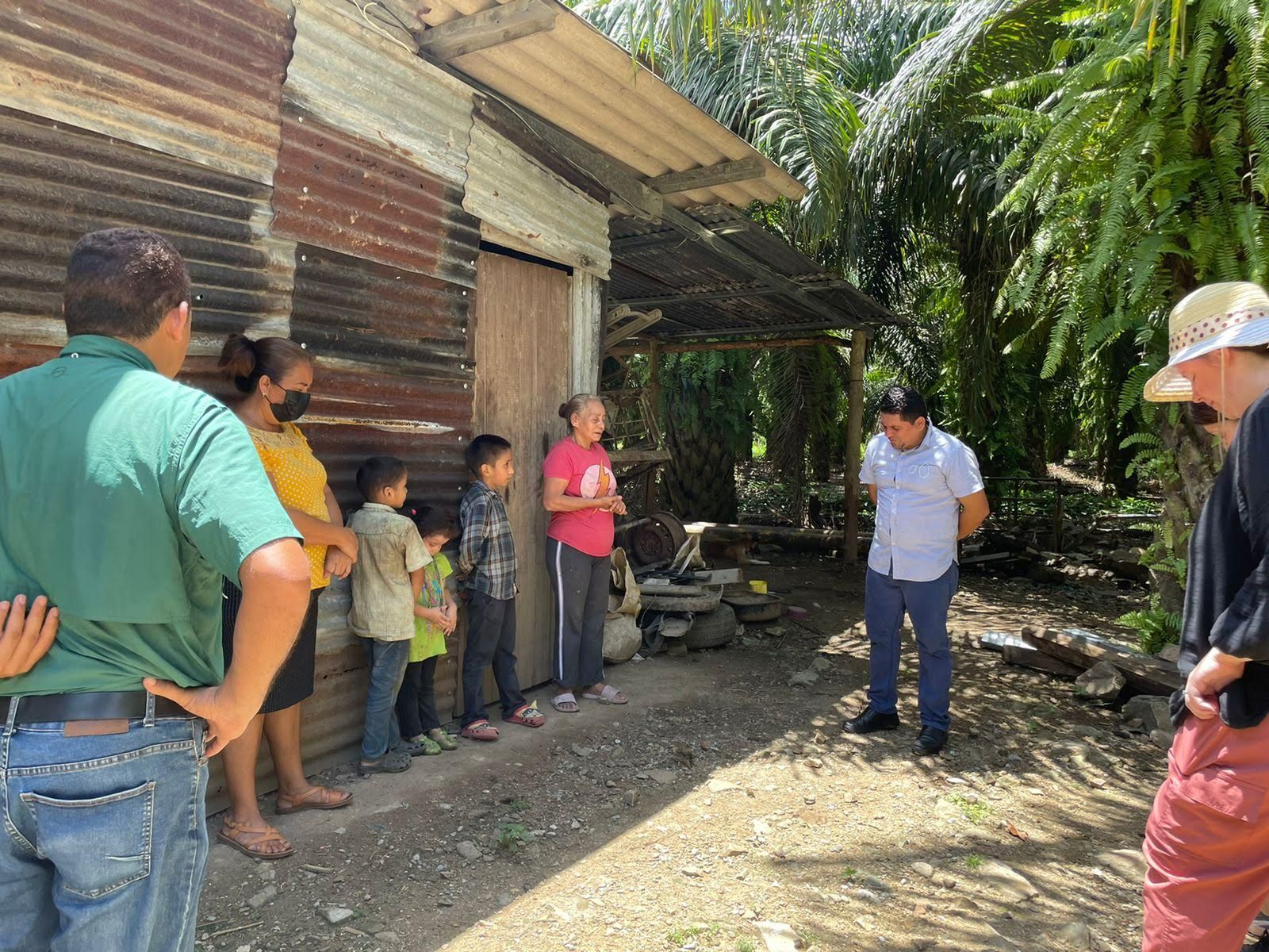 People standing outside a corrugated metal building in a sunny rural yard.
