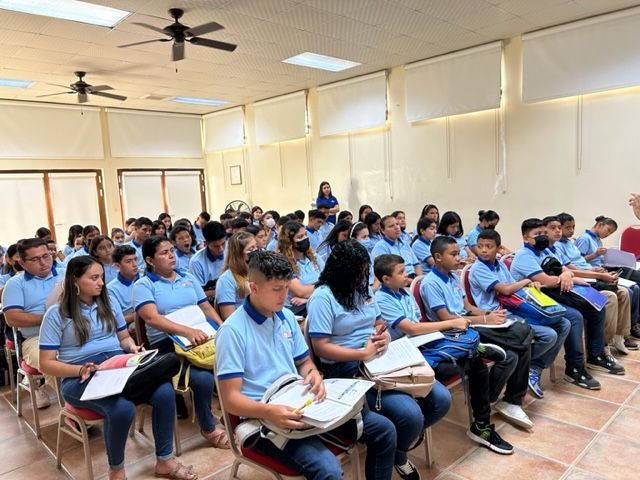 Students in blue shirts seated in a classroom, reading papers during a lesson.