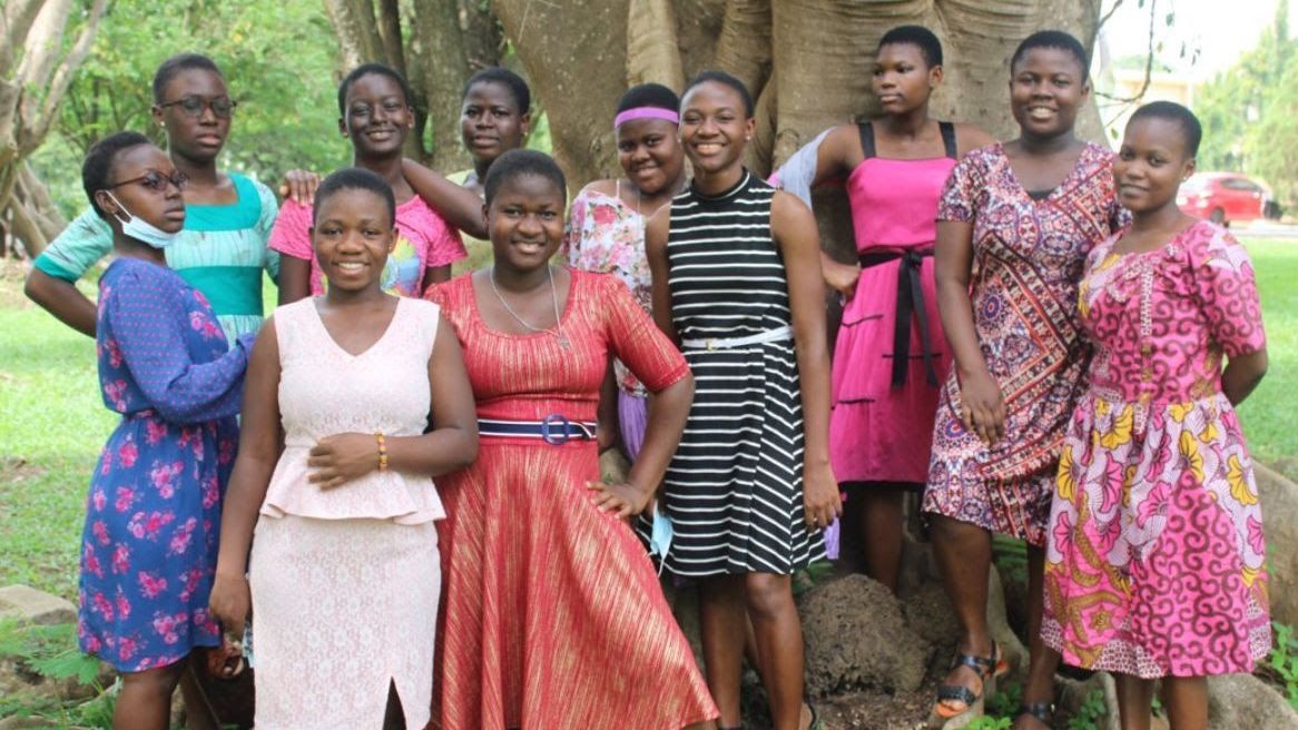 A group of young women are posing for a picture in front of a tree.