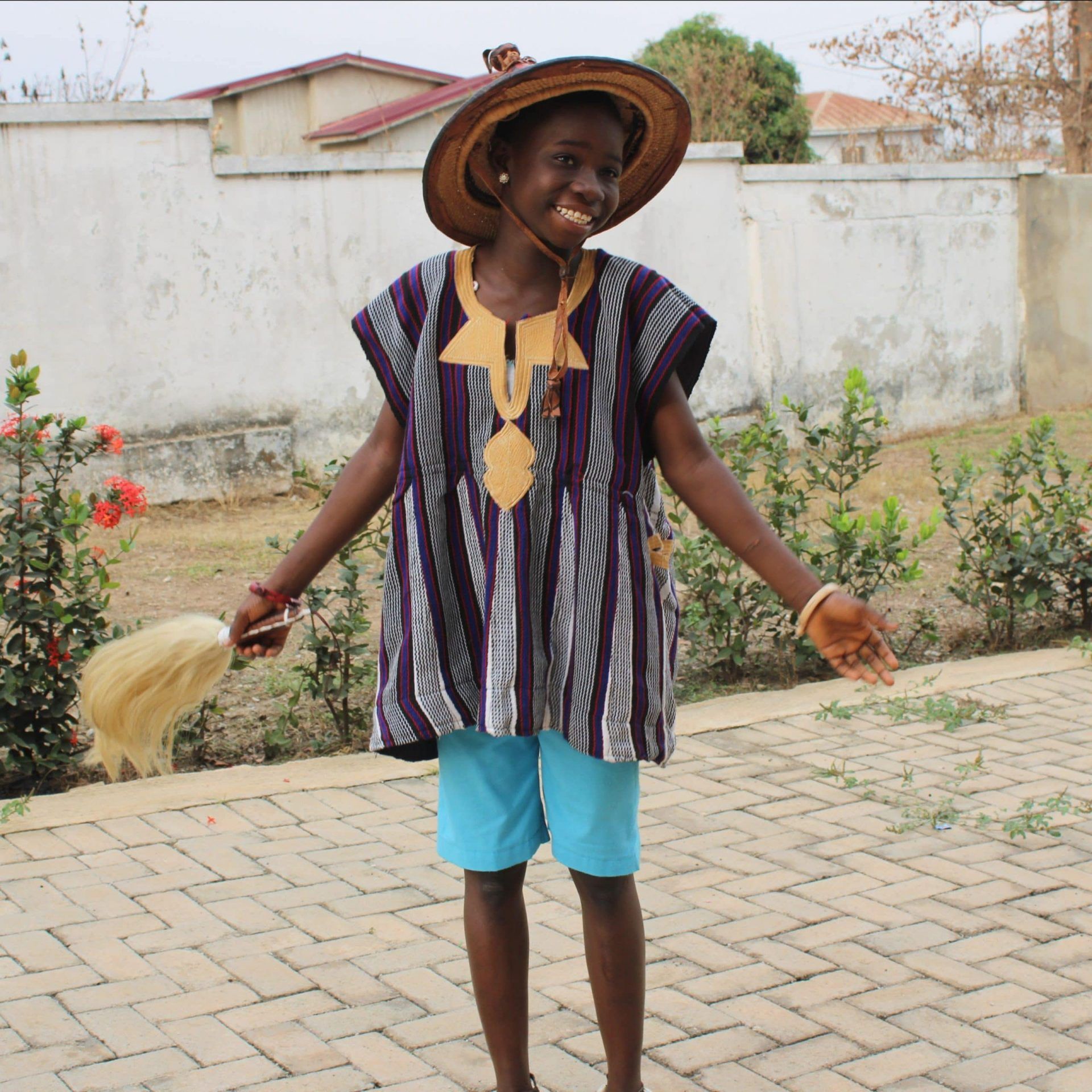 A girl wearing a hat and a striped shirt is standing on a brick sidewalk