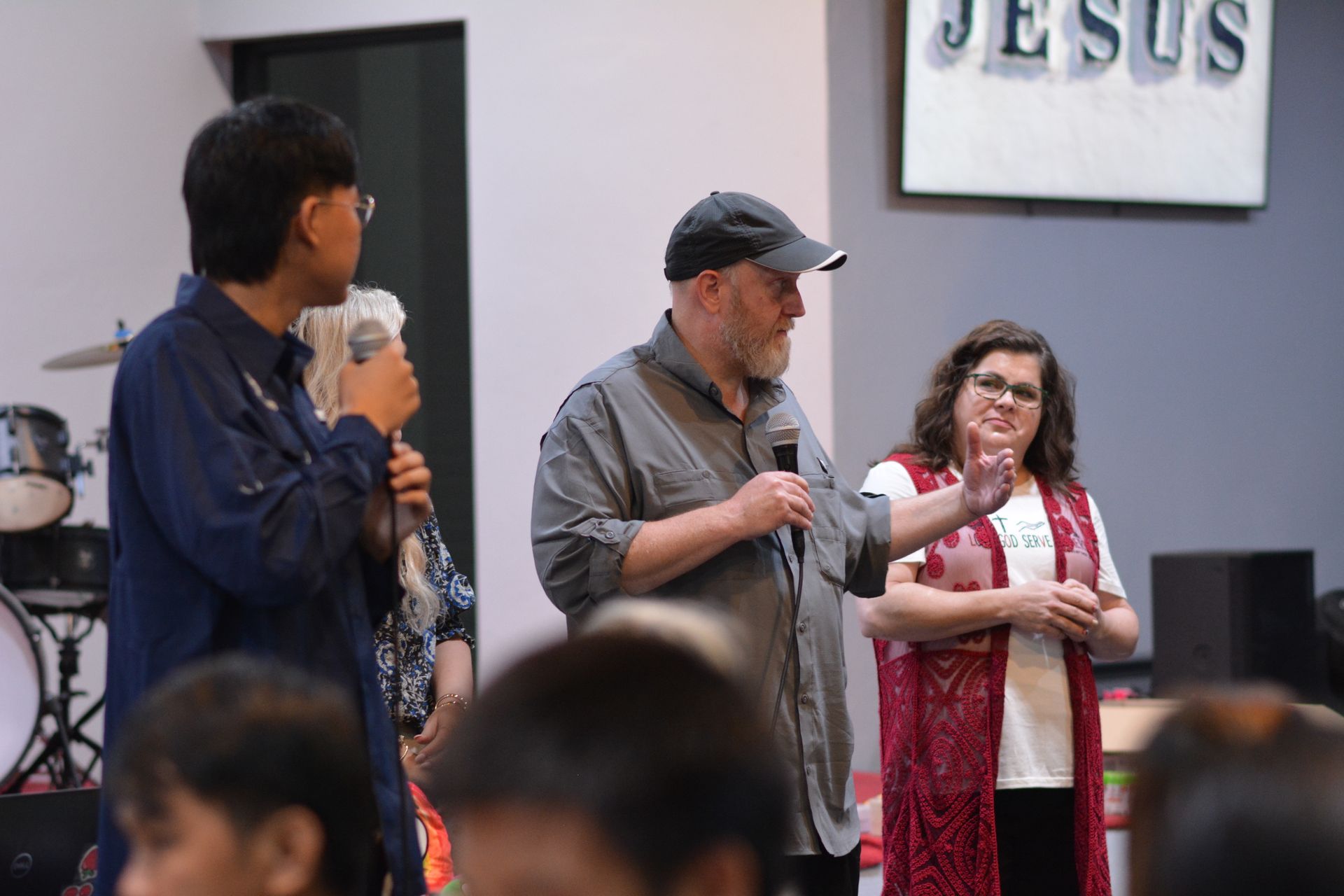 Three people speaking into microphones in a room with a 