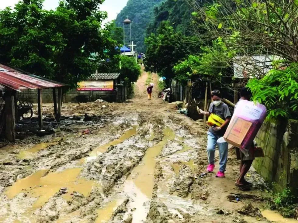 A man is carrying a box down a muddy road.