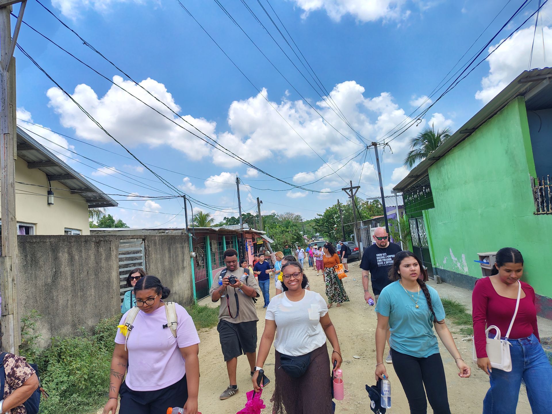 People walking down a narrow neighborhood street under a blue sky with power lines overhead