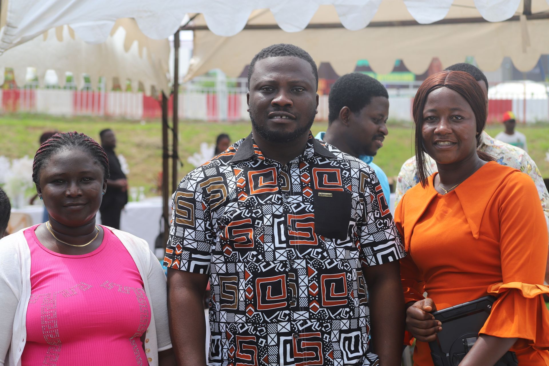 Three people standing under a white tent, posing at an outdoor event.