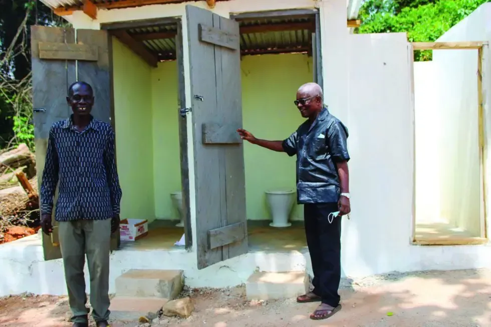 Two men are standing in front of a toilet.