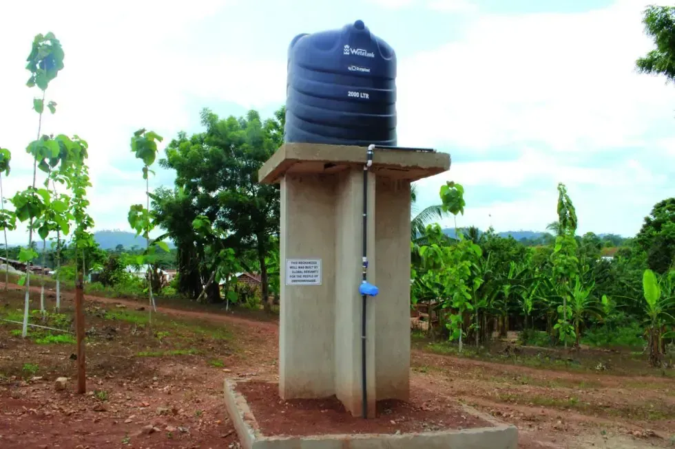 A black water tank sits on top of a concrete structure in a field