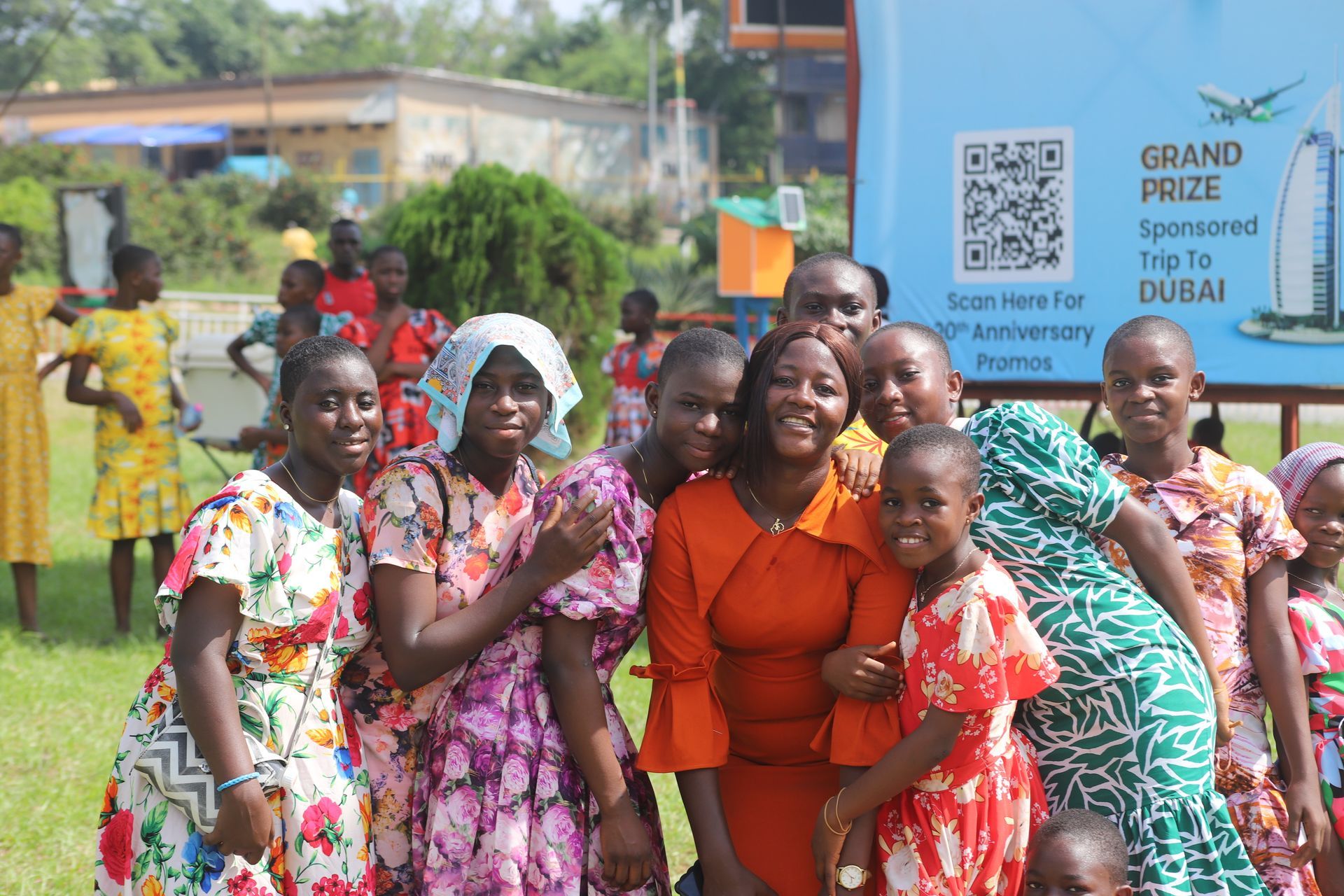 Group smiling beside a Grand Prize sponsor sign at an outdoor event, with colorful clothing and greenery.