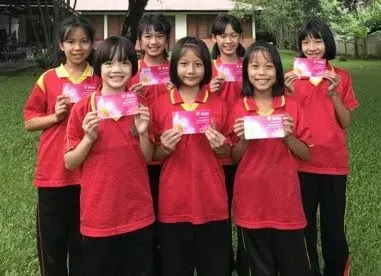 A group of young girls in red shirts are standing next to each other holding cards.