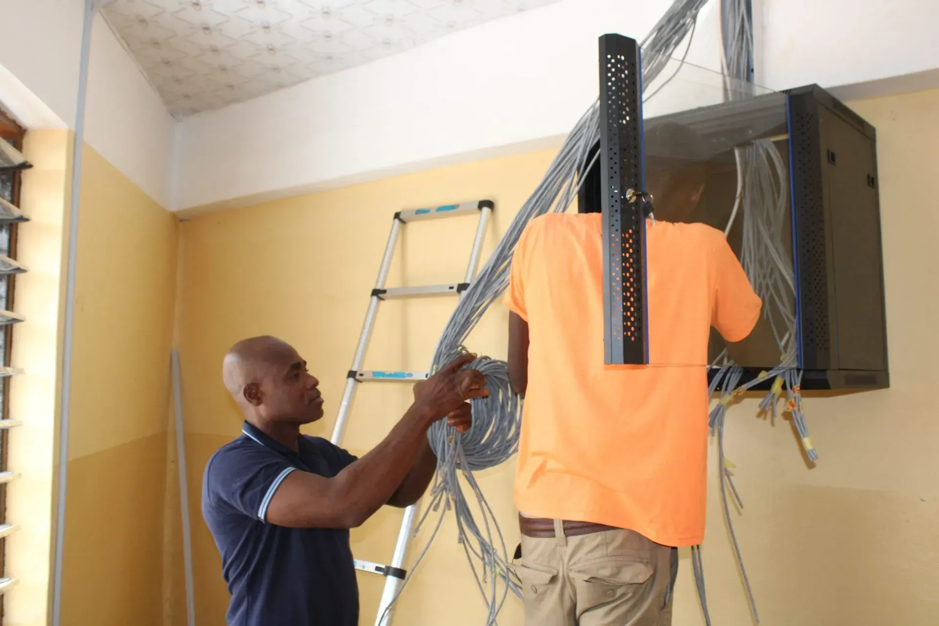 A man in an orange shirt is working on an electrical box