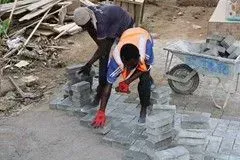 Two men are working on a sidewalk with bricks.