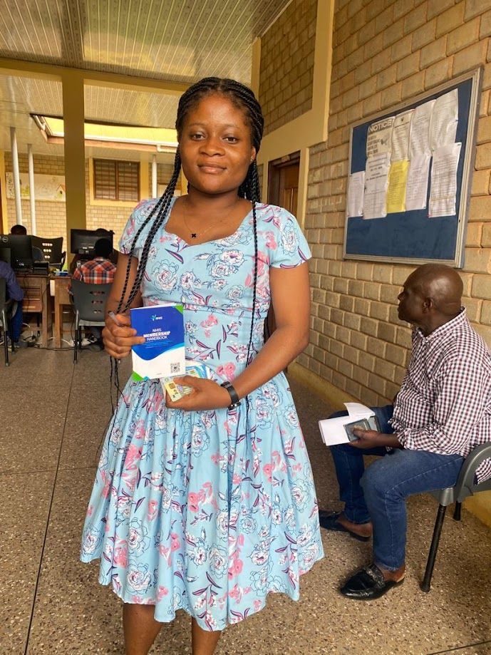 Woman in blue dress holding package, smiling; inside a building.