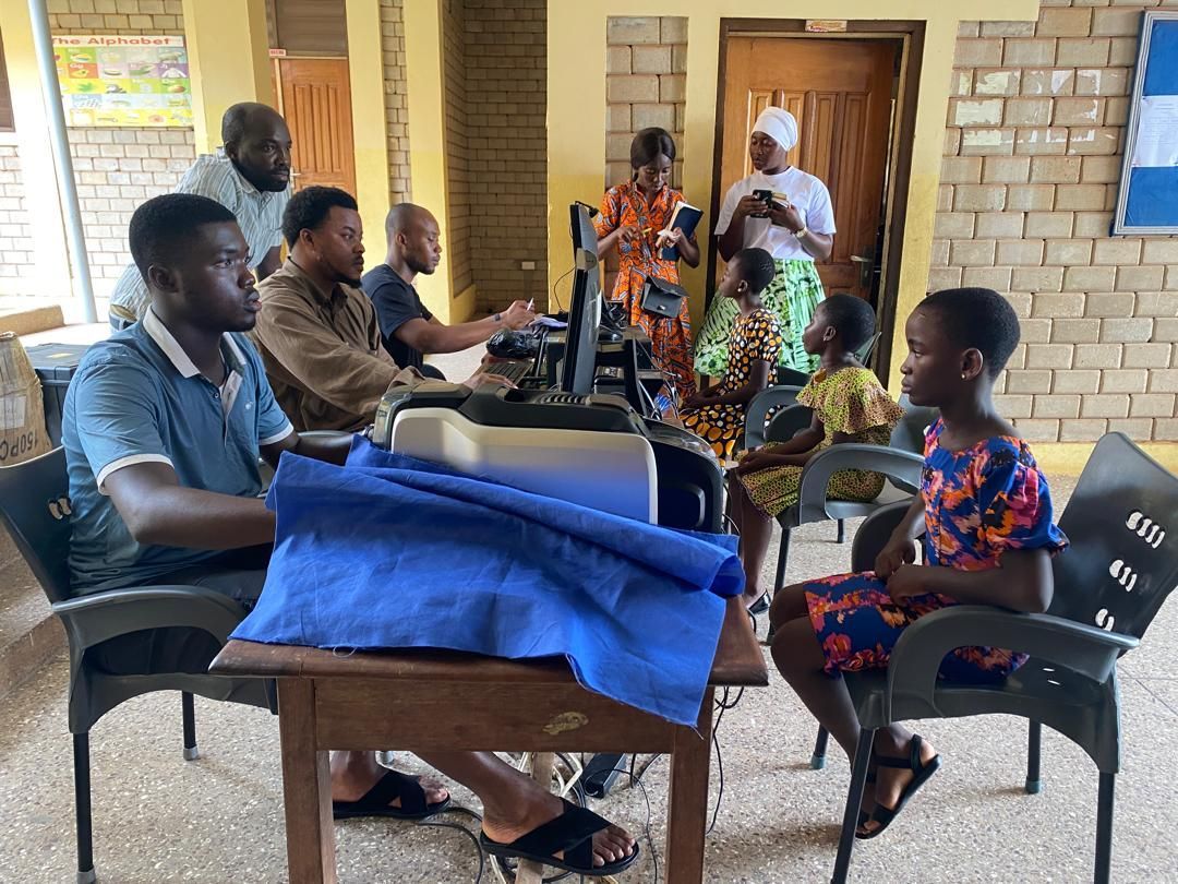 People gathered indoors, seated at tables, some looking at fabric; some are talking.