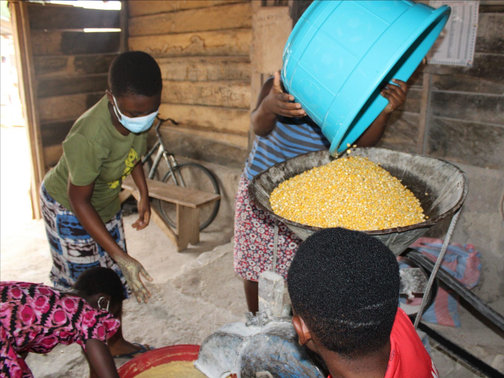 A man is pouring a blue bucket of corn into a bowl