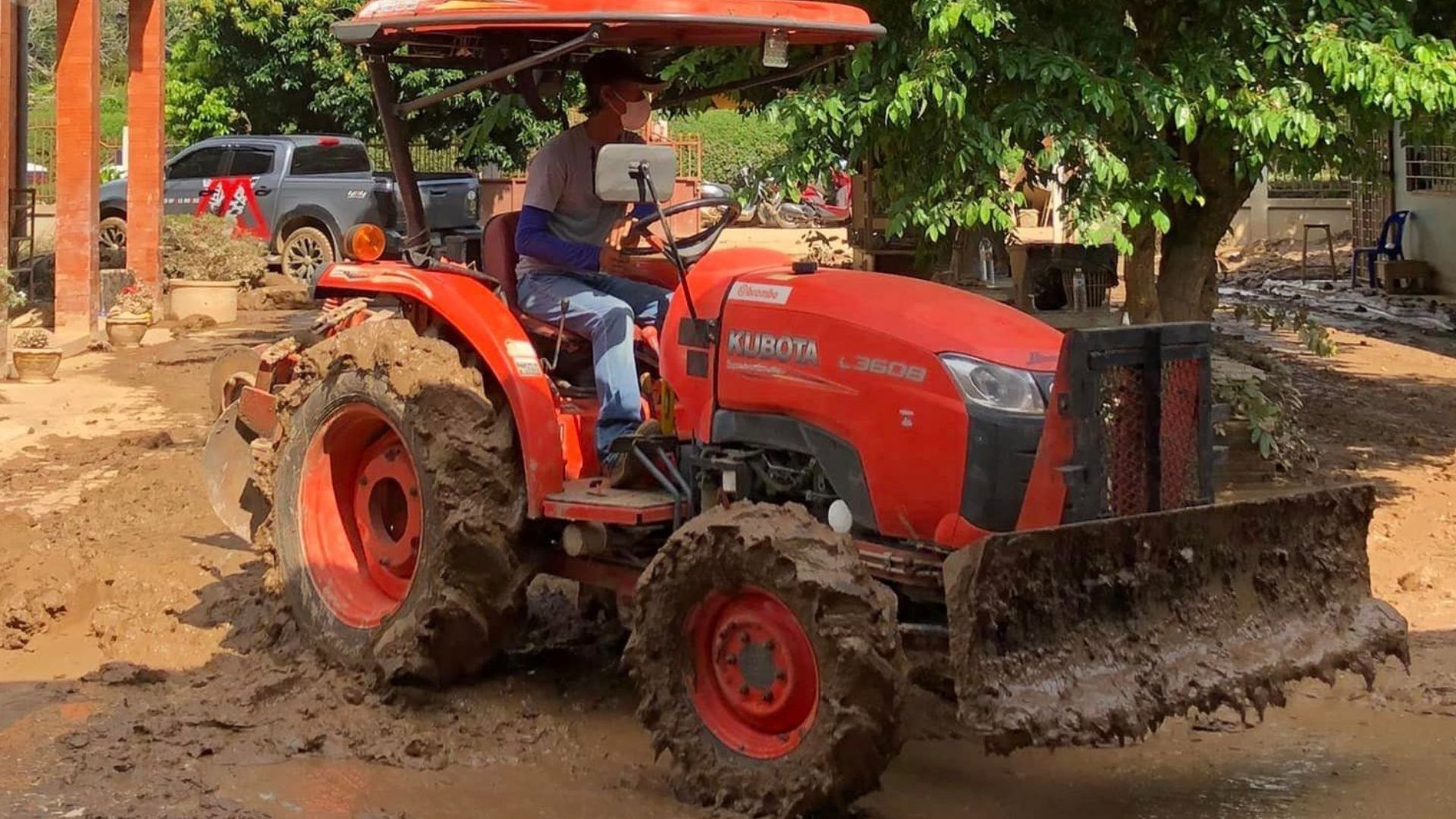 An orange tractor with a driver moves through muddy terrain, clearing debris.