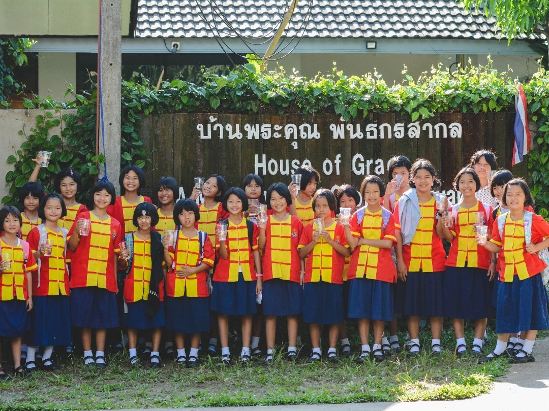 Group of schoolgirls in uniforms standing in front of a sign that reads 