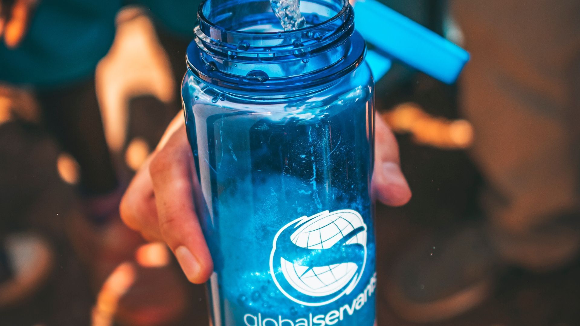 Hand pouring water into a blue water bottle with a logo reading 