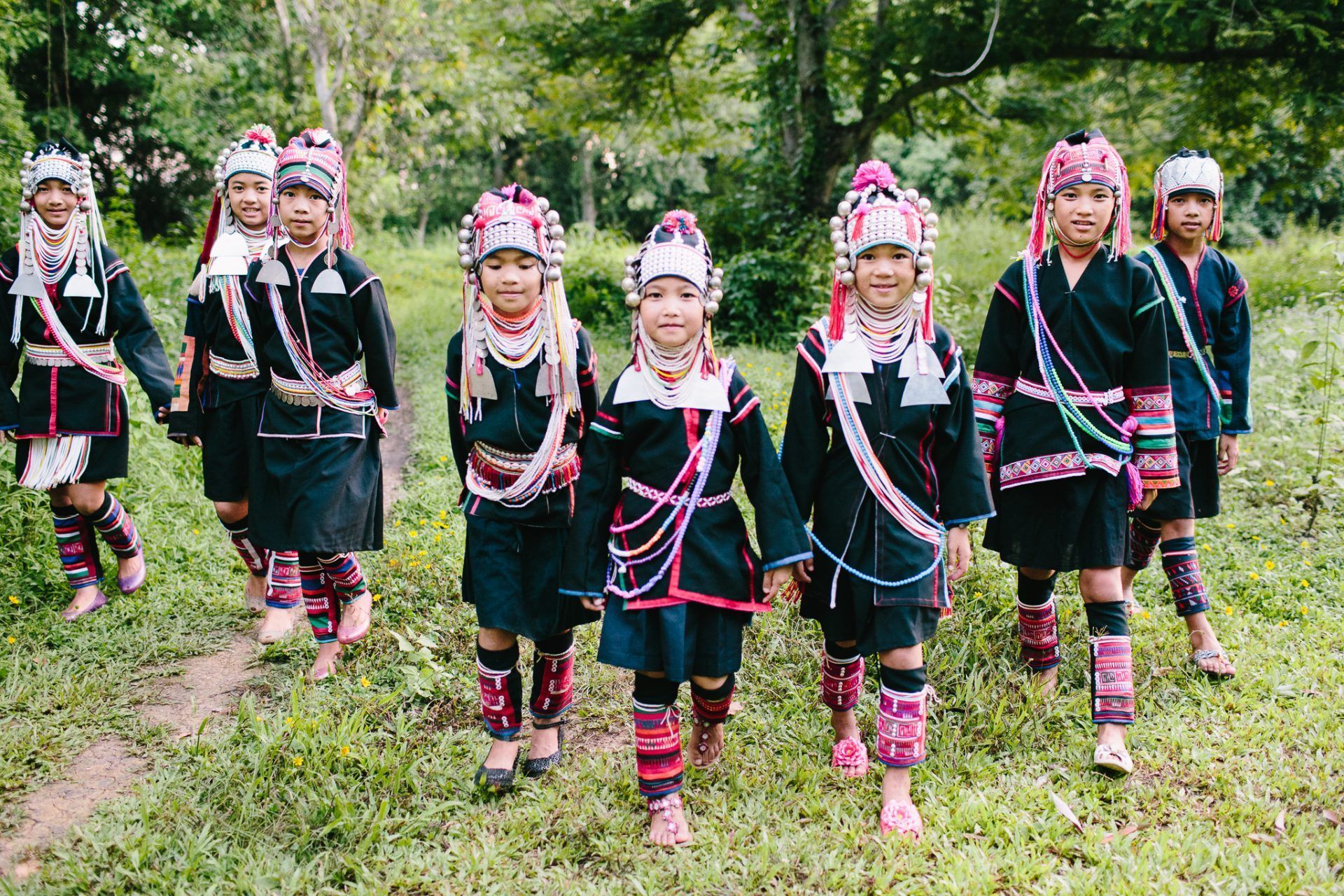 A group of children in traditional costumes are walking through a grassy field.