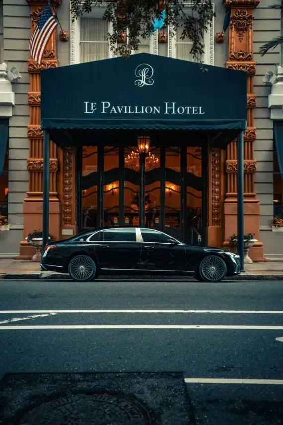 A black Mercedes-Maybach sedan parked on a city street next to a tall grey building and a vibrant red building.