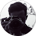 A close-up circular portrait of a person holding a DSLR camera up to their face, obscuring their features.