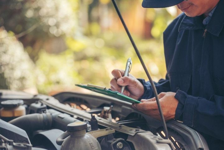 Mechanic writing notes while inspecting a car engine with the hood open