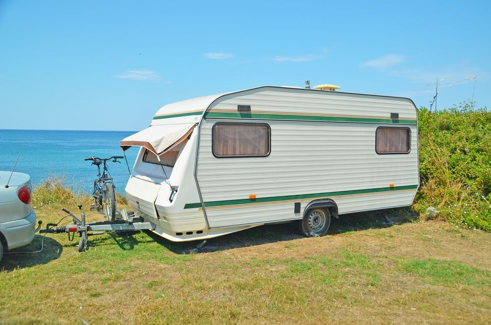 A Caravan Is Parked Next To A Car In A Grassy Area Near The Ocean — Kingston Caravan Repairs In Newcastle, NSW