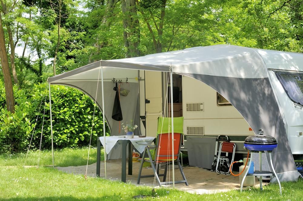 A Camper Is Parked In A Grassy Field With A Table And Chairs Under A Canopy — Kingston Caravan Repairs In Heatherbrae, NSW