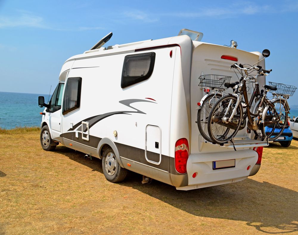 A White Caravan With Two Bikes On The Back Is Parked On A Beach — Kingston Caravan Repairs In Heatherbrae, NSW