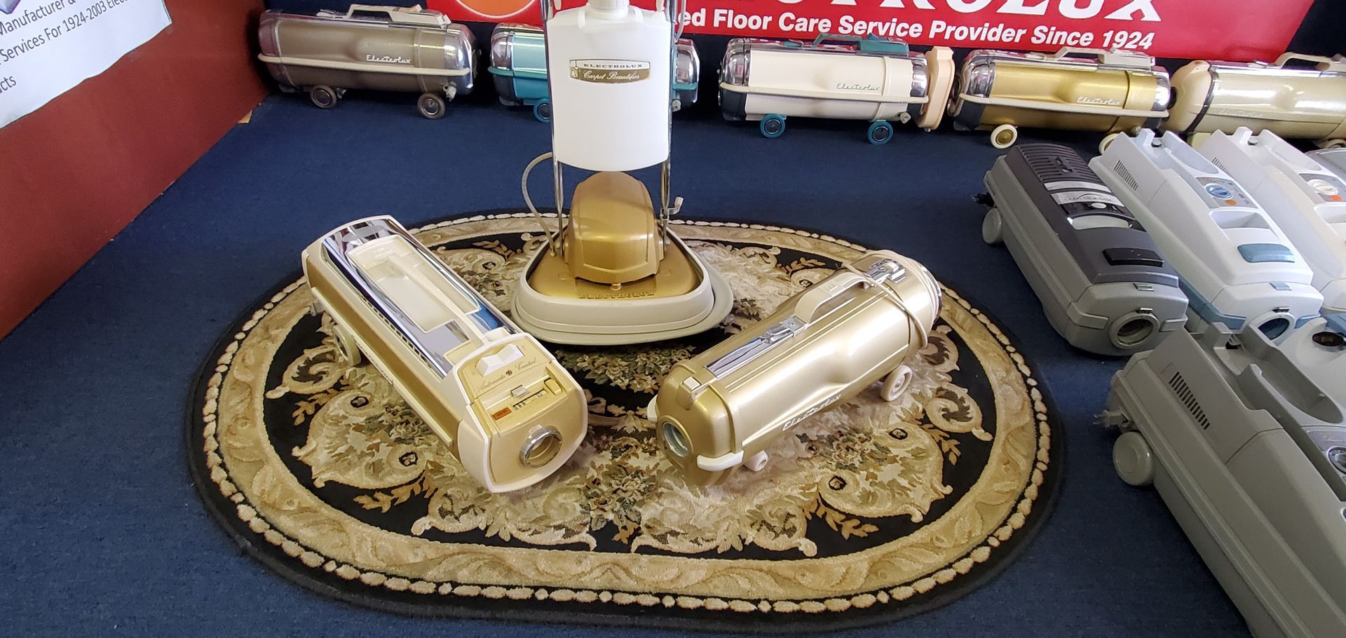 Display of toy train cars and a locomotive on a patterned rug with a white cylindrical object in the center