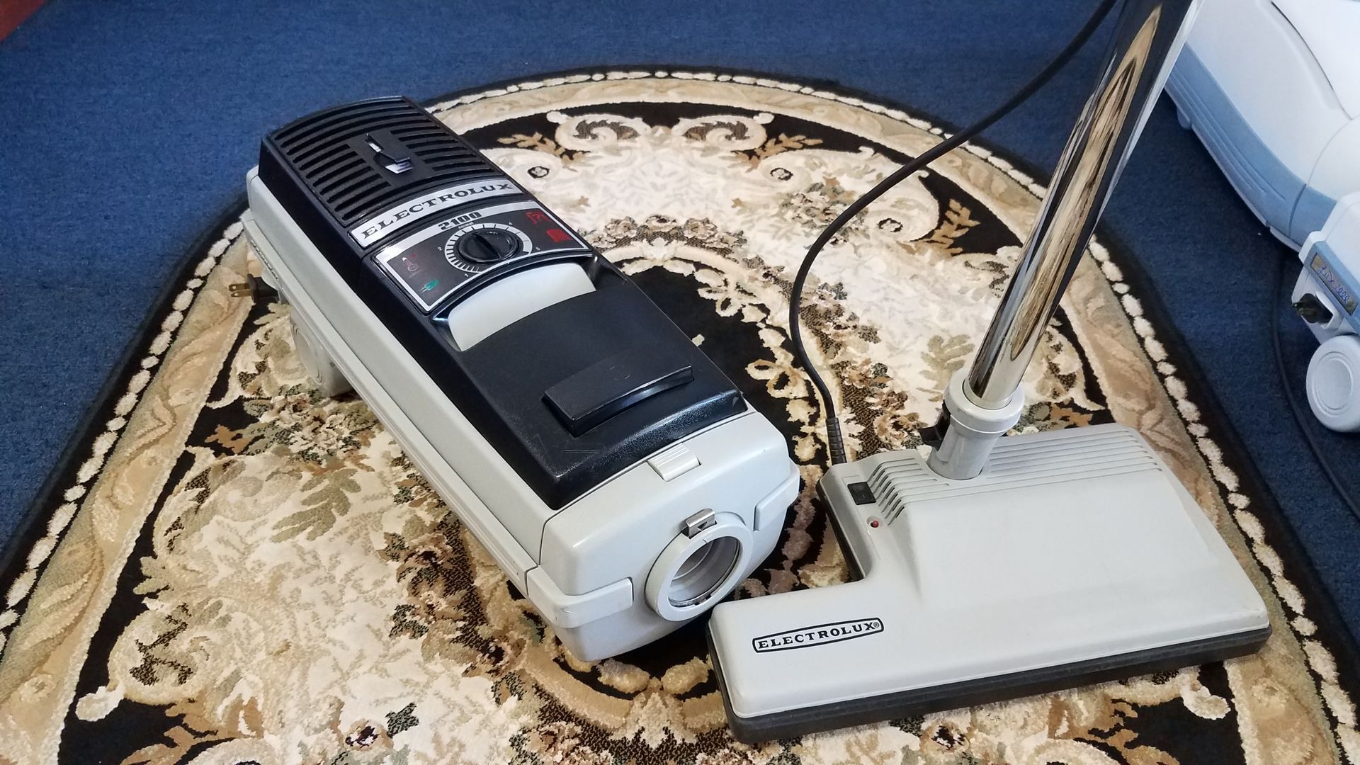 A carpeted floor with a white and black device beside a small white antenna base.