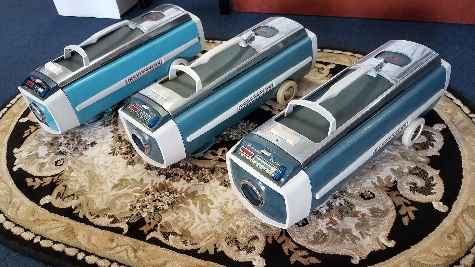 Three blue-and-silver cylindrical devices displayed on a patterned cloth runner.