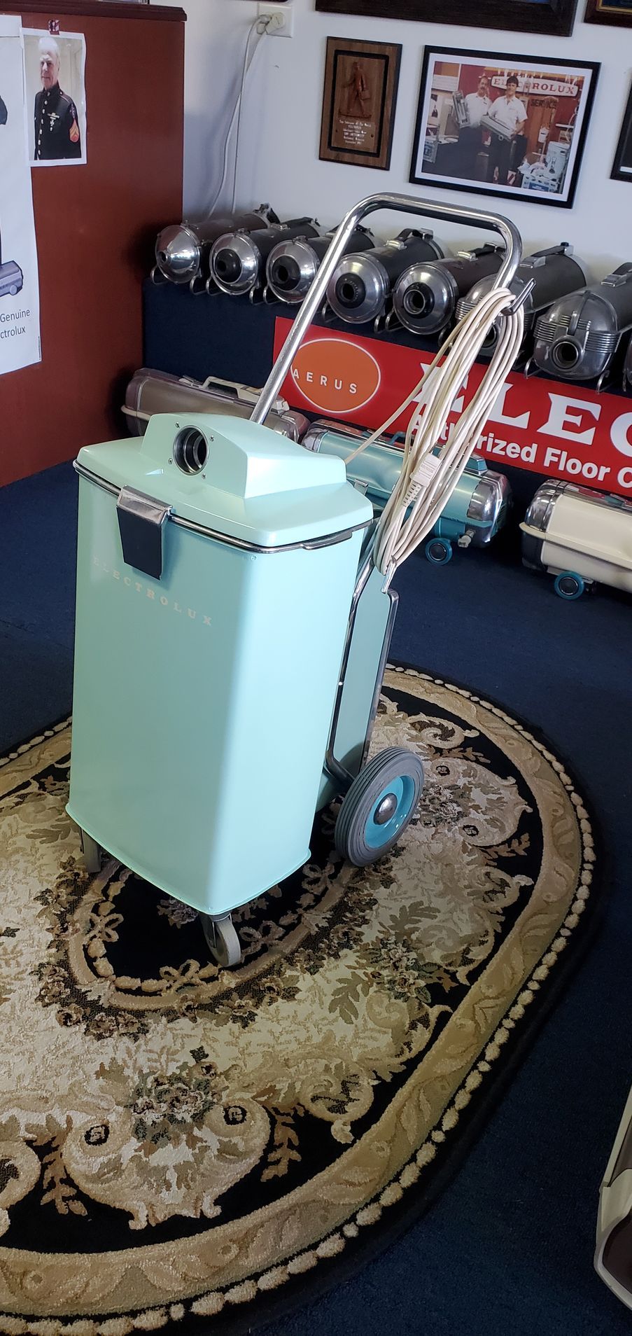 Vintage mint-green wheeled machine with metal top, displayed on an oval rug in a room.