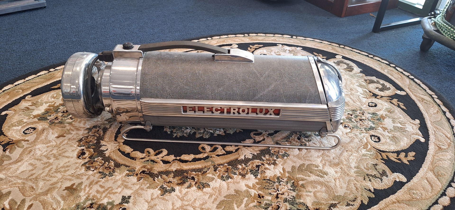 Chrome vacuum cleaner head on a patterned rug in a room with a blue floor.